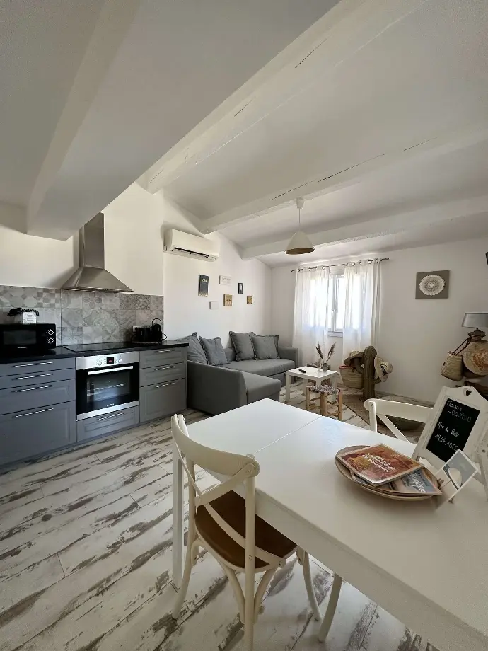 Cuisine et salon confortables de la location de vacances Loc'Amargue avec électroménager moderne, sol blanchi à la chaux et canapé gris confortable aux Saintes-Maries-de-la-Mer.