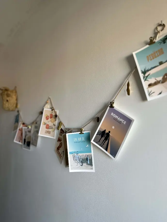 Décoration murale artistique avec des cartes postales sur un fil suspendu et des pinces dorées à Loc'Amargue aux Saintes-Maries-de-la-Mer