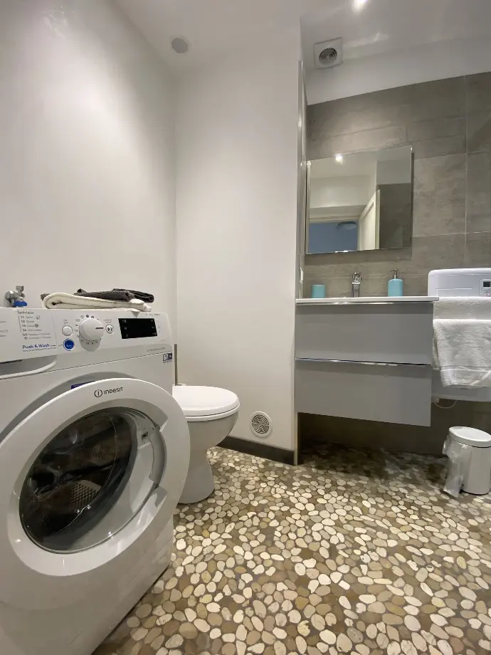 Salle d'eau fonctionnelle avec lave-linge, toilettes et vasque surmontée d'un miroir, sol en galet à Loc'Amargue, Saintes-Maries-de-la-Mer