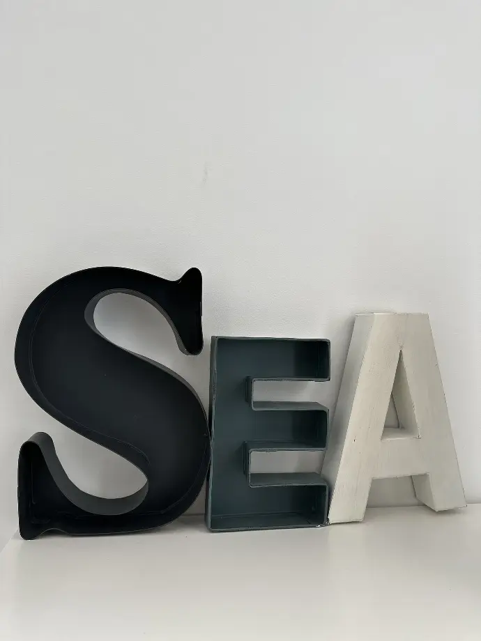 Lettres décoratives formant le mot 'SEA' en noir, vert et blanc sur un fond clair à Loc'Amargue, Saintes-Maries-de-la-Mer