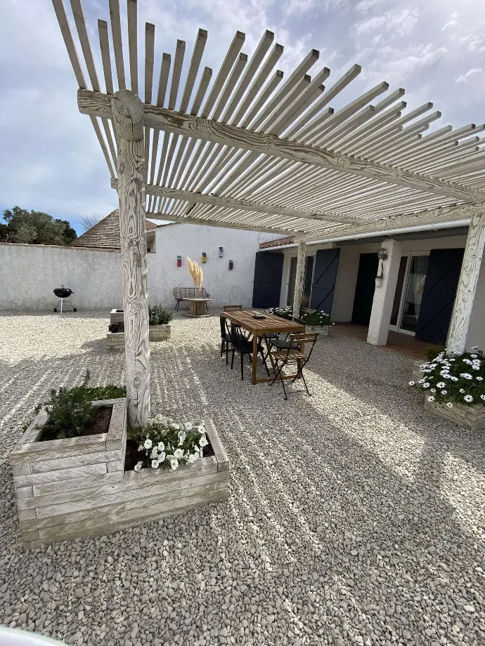 Cour intérieure en gravier avec pergola en bois, table rustique et plantes, à Loc'Amargue, Saintes-Maries-de-la-Mer