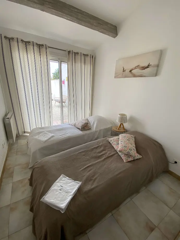 Chambre lumineuse avec deux lits simples, couvertures marron, et porte-fenêtre donnant sur l'extérieur au Mas des Oliviers, Loc'Amargue, Saintes-Maries-de-la-Mer