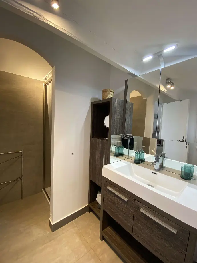 Salle de bain moderne avec grand miroir, meuble vasque en bois foncé, et éclairage encastré au Mas des Oliviers, Loc'Amargue, Saintes-Maries-de-la-Mer