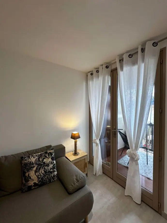 Salon lumineux avec canapé confortable, lampe de chevet et rideaux blancs donnant sur une terrasse privée