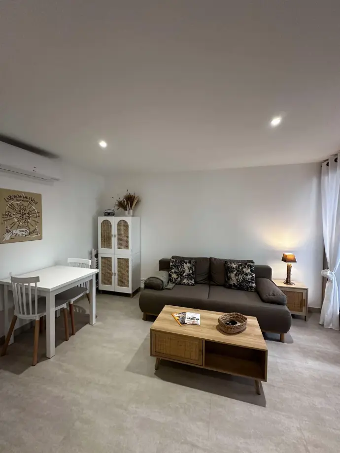 Salon moderne et lumineux d'un appartement avec canapé confortable, table à manger blanche et mobilier en bois aux accents naturels, situé dans une résidence privée aux Saintes-Maries-de-la-Mer