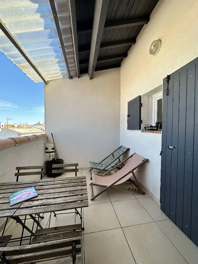 Balcon accueillant pour se détendre à Loc’Amargue, Saintes-Maries-de-la-Mer Balcon confortable de l’appartement de vacances Loc’Amargue avec une table en bois, des chaises et un ciel dégagé en arrière-plan