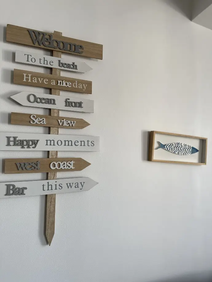 Panneau décoratif en bois avec flèches directionnelles et inscriptions accueillantes, à côté d'une illustration de poisson, chez Loc'Amargue