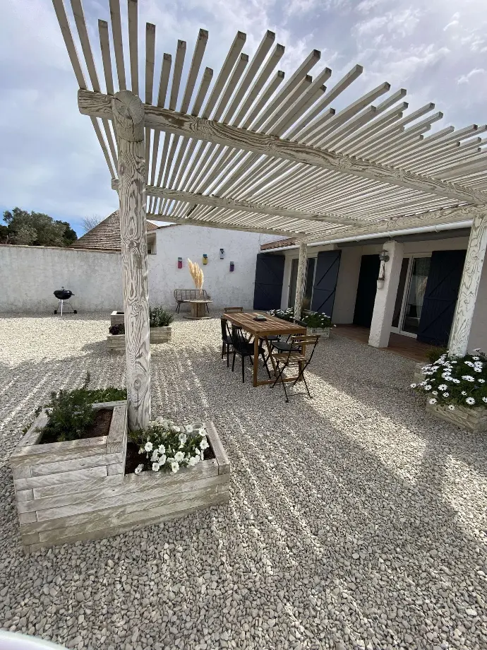 Espace extérieur chaleureux avec pergola à Loc'Amargue - Détente aux Saintes-Maries-de-la-Mer Cour intérieure en gravier avec pergola en bois, table rustique et plantes, à Loc'Amargue, Saintes-Maries-de-la-Mer