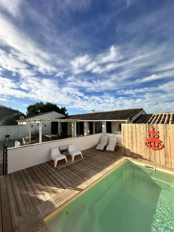 Vue sur la piscine éclairée par le soleil avec des chaises longues, entourée d’une belle maison de vacances à Loc’Amargue aux Saintes Maries de la Mer